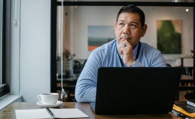 thoughtful ethnic businessman using laptop while working in office